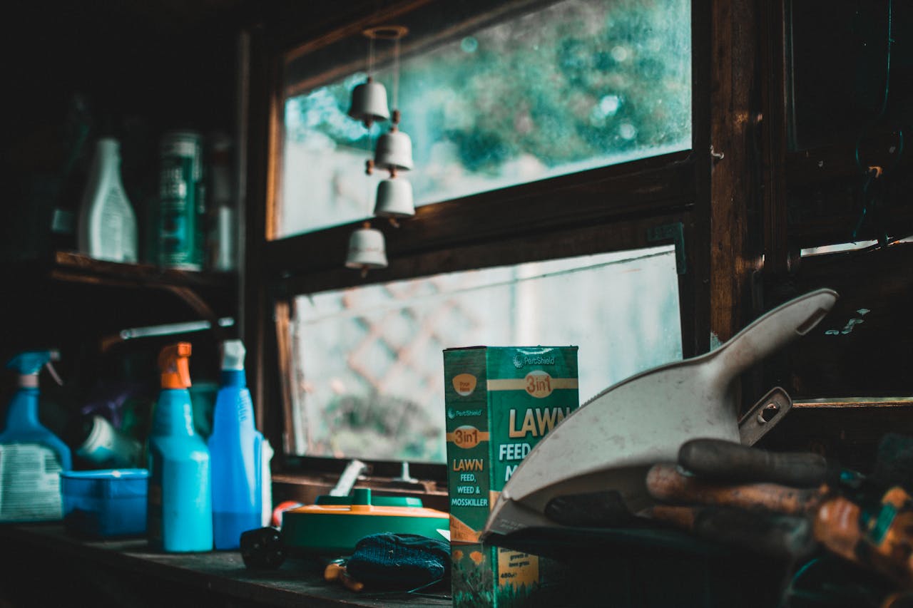 A cozy indoor garden shed scene with tools and lawn supplies by a window.