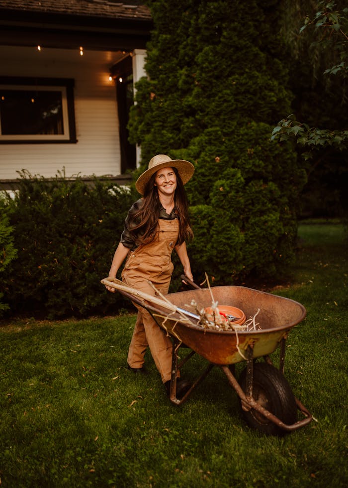 A smiling woman gardener with a straw hat tends to garden tasks at dusk.